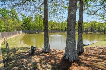 the pond is surrounded by trees and a fence at Reserve of Jackson Apartment Homes, Mississippi